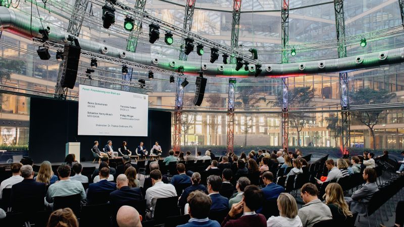 Sitzendes Publikum in einem Glaskuppel-Konferenzraum vor Personen auf einer Bühne 