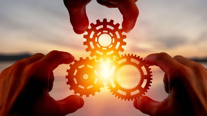 Drei Zahnräder gehalten von Fingern mit Sonne im Hintergrund