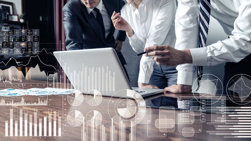 Drei Männer vor einem Laptop und eingeblendete Diagramme