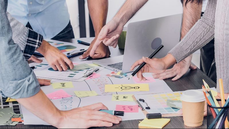 Personen stehen und deuten auf einen Plan auf einem Tisch