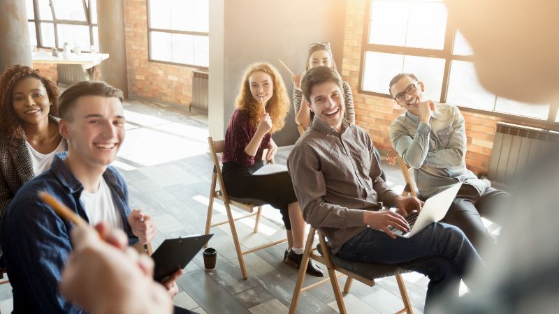Drei Männer und drei Frauen sitzen lachend auf Stühlen