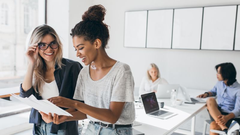 Zwei Frauen im Gespräch und im Hintergrund zwei Frauen an Tisch sitzend