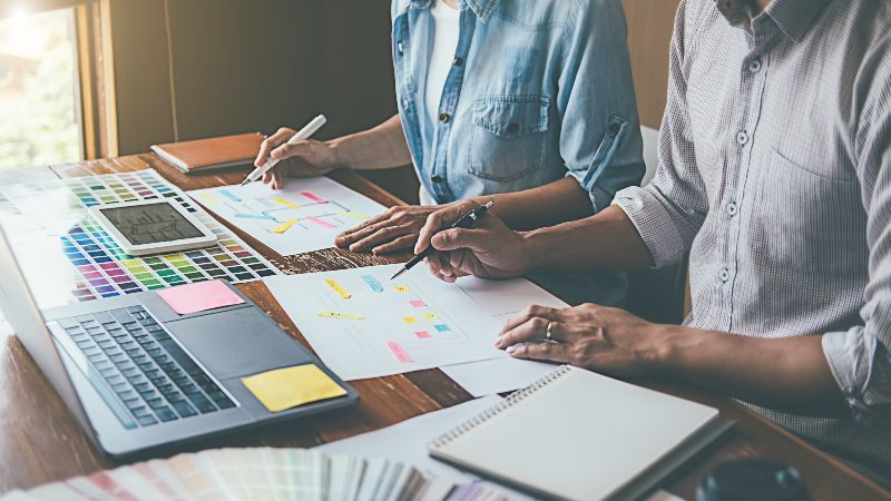 Zwei Personen mit Schreibstiften sitzend mit Laptop