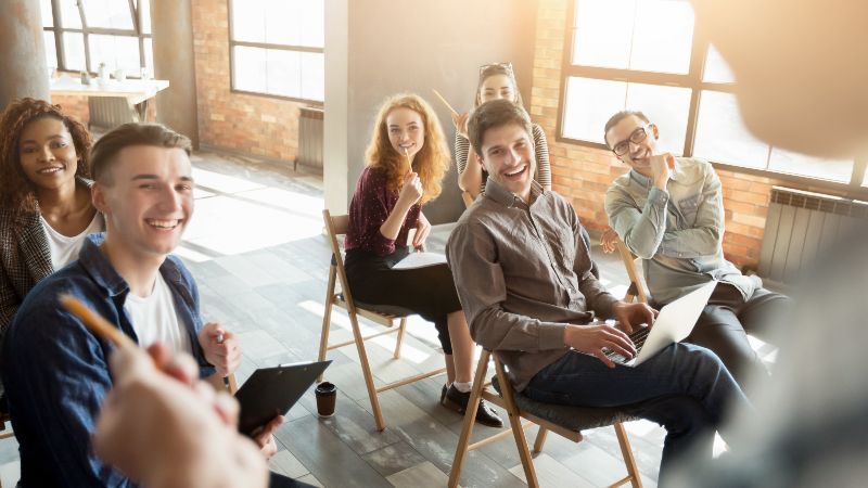 Drei Männer und drei Frauen sitzen lachend auf Stühlen