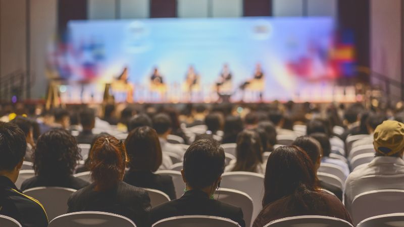 Rückansicht des Publikums, das den Rednern auf der Bühne zuhört