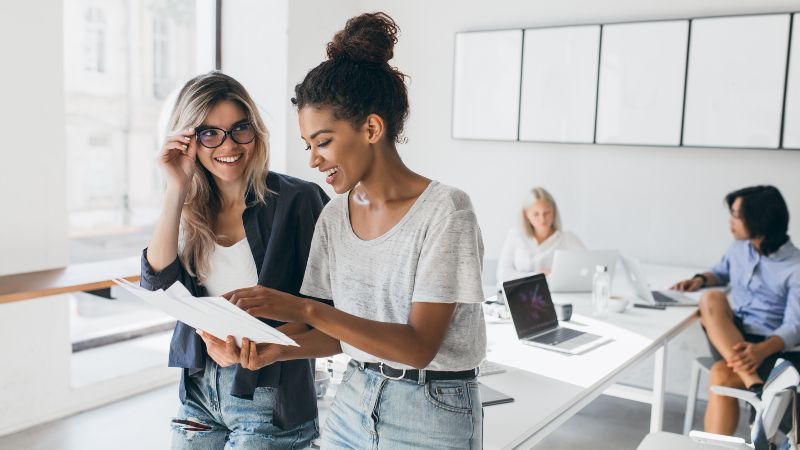 Zwei Frauen im Gespräch und im Hintergrund zwei Frauen an Tisch sitzend