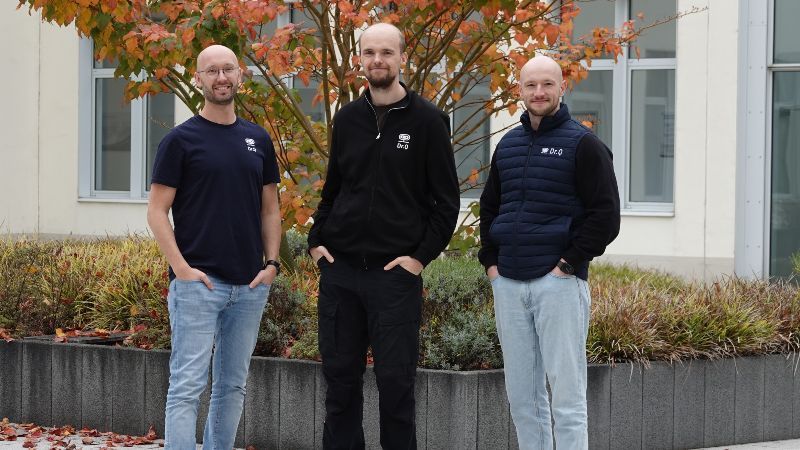 Drei Gründer stehen vor einem Gebäude und blicken in die Kamera
