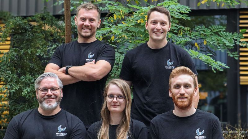 Vier Gründer und eine Mitarbeiterin tragen schwarze T-Shirts mit dem Firmenlogo und lächeln in die Kamera