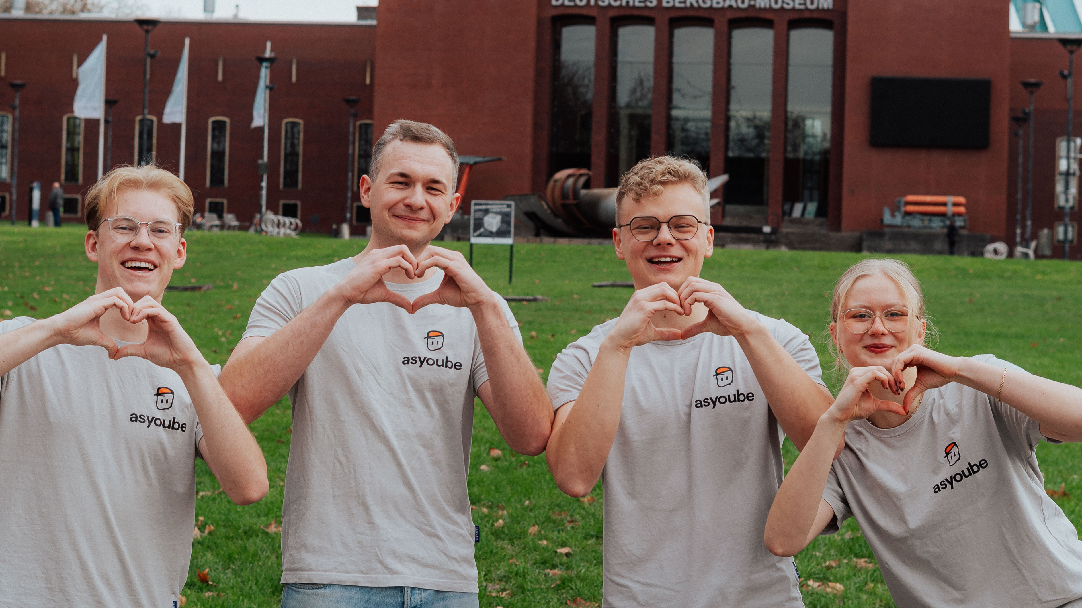 Die beiden Gründer und ihre beiden Mitarbeitenden tragen T-Shirts mit dem Firmenlogo, formen Herzen mit ihren Händen und lächeln in die Kamera