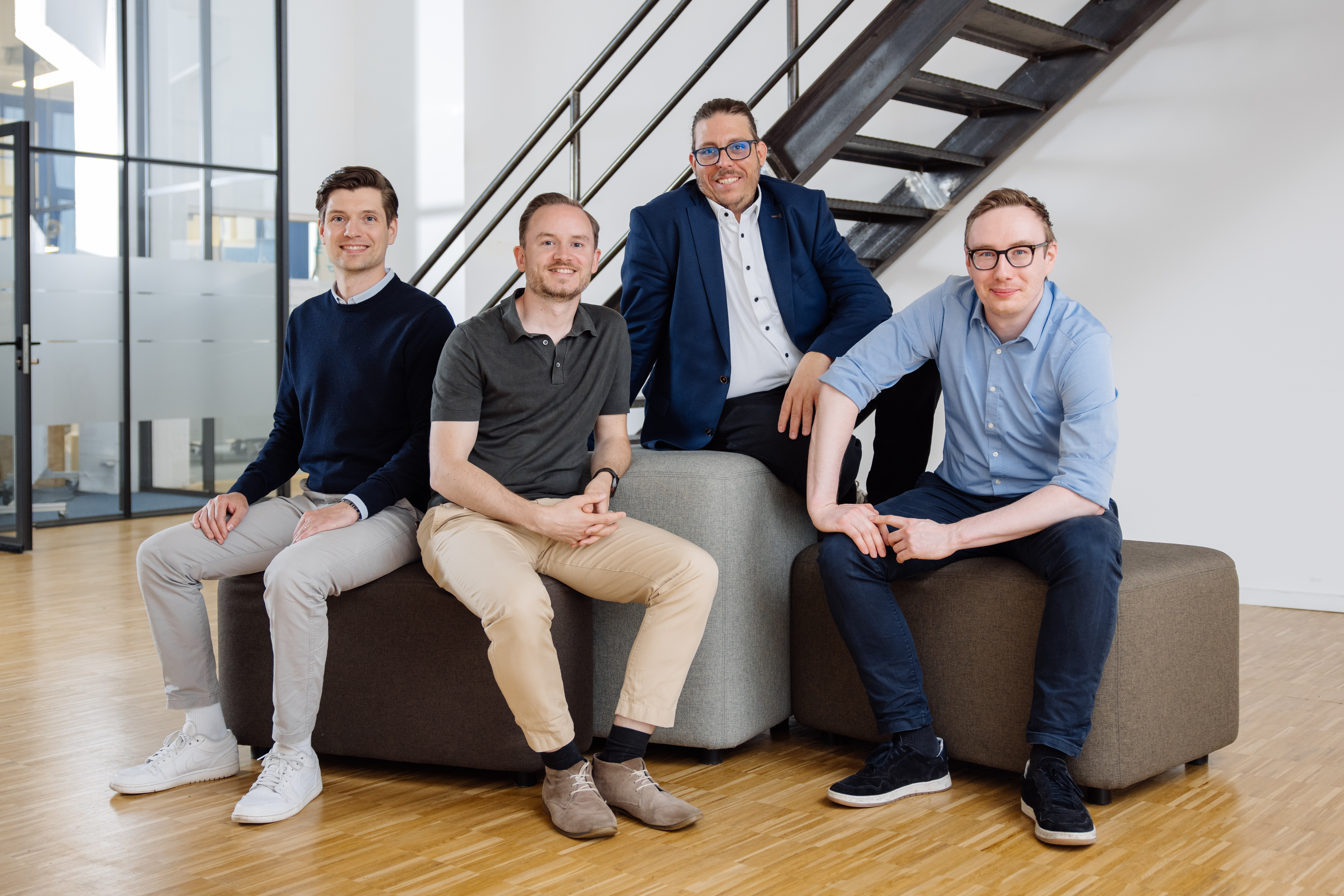 Die vier Gründer sitzen auf Sitzwürfeln und lächeln in die Kamera.