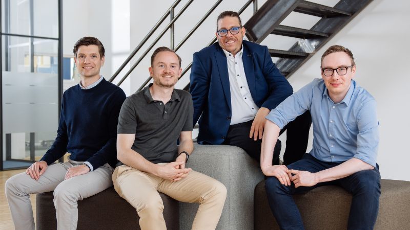 Die vier Gründer sitzen auf Sitzwürfeln und lächeln in die Kamera.