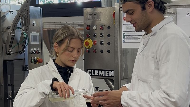 Nina Moritz und ihr Mitarbeiter Robin Trujillo Meyer stehen im Labor in weißen Kitteln und füllen eine Flüssigkeit ab.