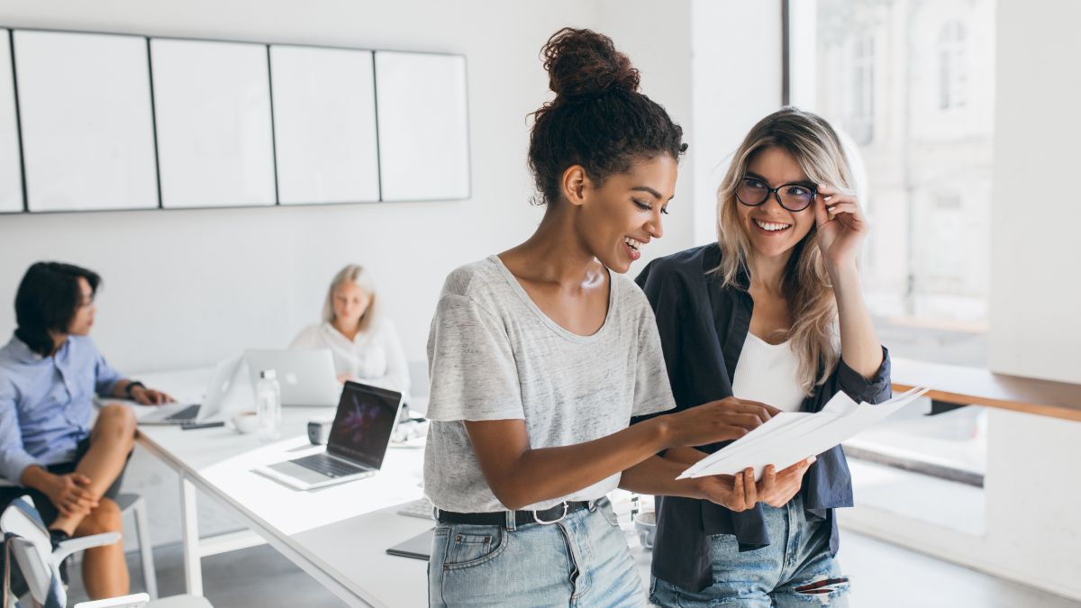 Zwei Frauen im Gespräch und im Hintergrund zwei Frauen an Tisch sitzend