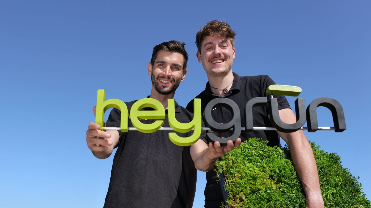Die beiden Gründer haben das Logo von heygrün in der Hand und lächeln in die Kamera.
