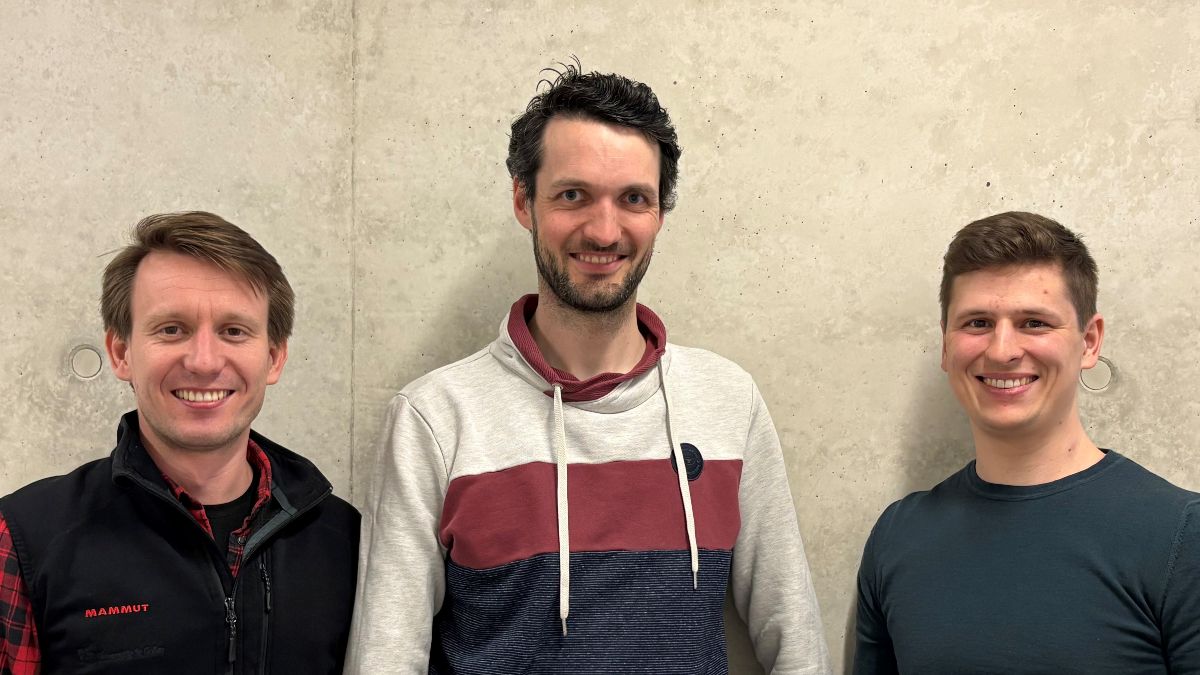 Drei junge Männer stehen vor einer Wand und blicken freundlich in die Kamera.