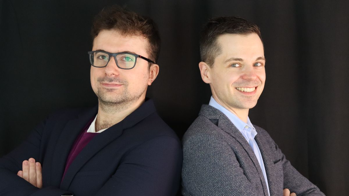 Zwei junge Männer stehen Rücken an Rücken und lächeln in die Kamera