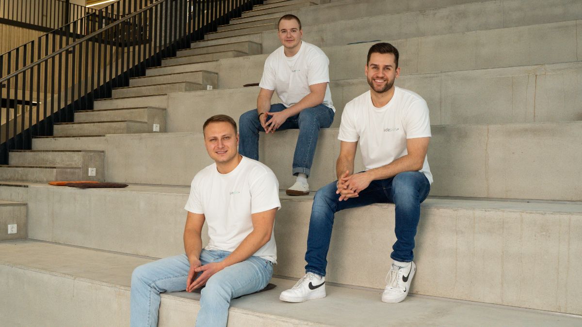 Die drei jungen Gründer sitzen auf Treppenstufen in der Aula der garage33